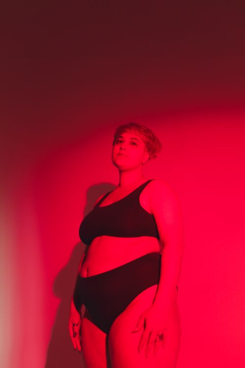 Free Empowering image of a plus size woman in moody red lighting, celebrating body positivity. Stock Photo