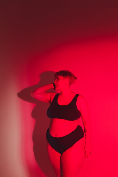 Free Studio shot of a confident plus-size woman in black lingerie illuminated by dramatic red lighting. Stock Photo