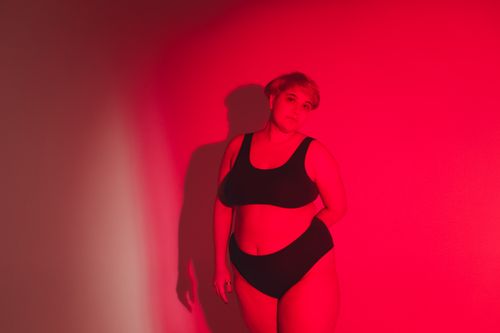 Free A confident woman poses in red lighting, celebrating body positivity in a studio setting. Stock Photo
