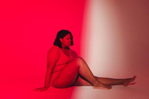 Free A plus size woman in a studio setting, embraced by vibrant red and pink lights, celebrating body positivity. Stock Photo