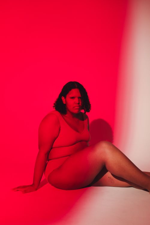 Free A confident plus size woman seated in a studio with dramatic red lighting. Stock Photo