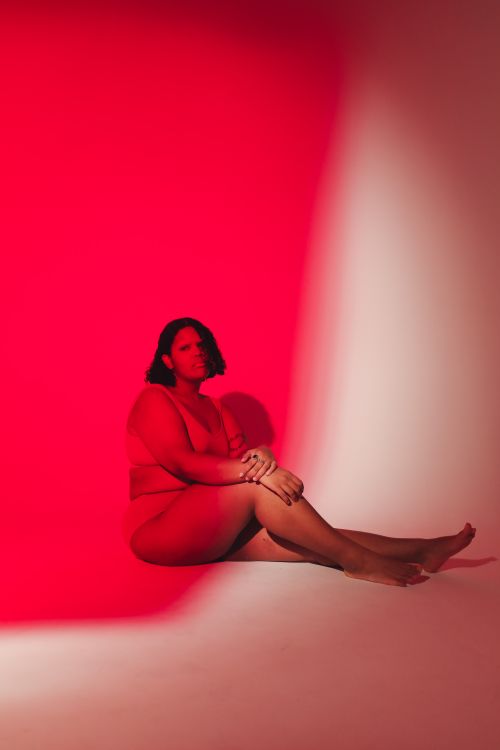 Free Plus-size woman sitting confidently in a red-lit studio, embracing body positivity. Stock Photo