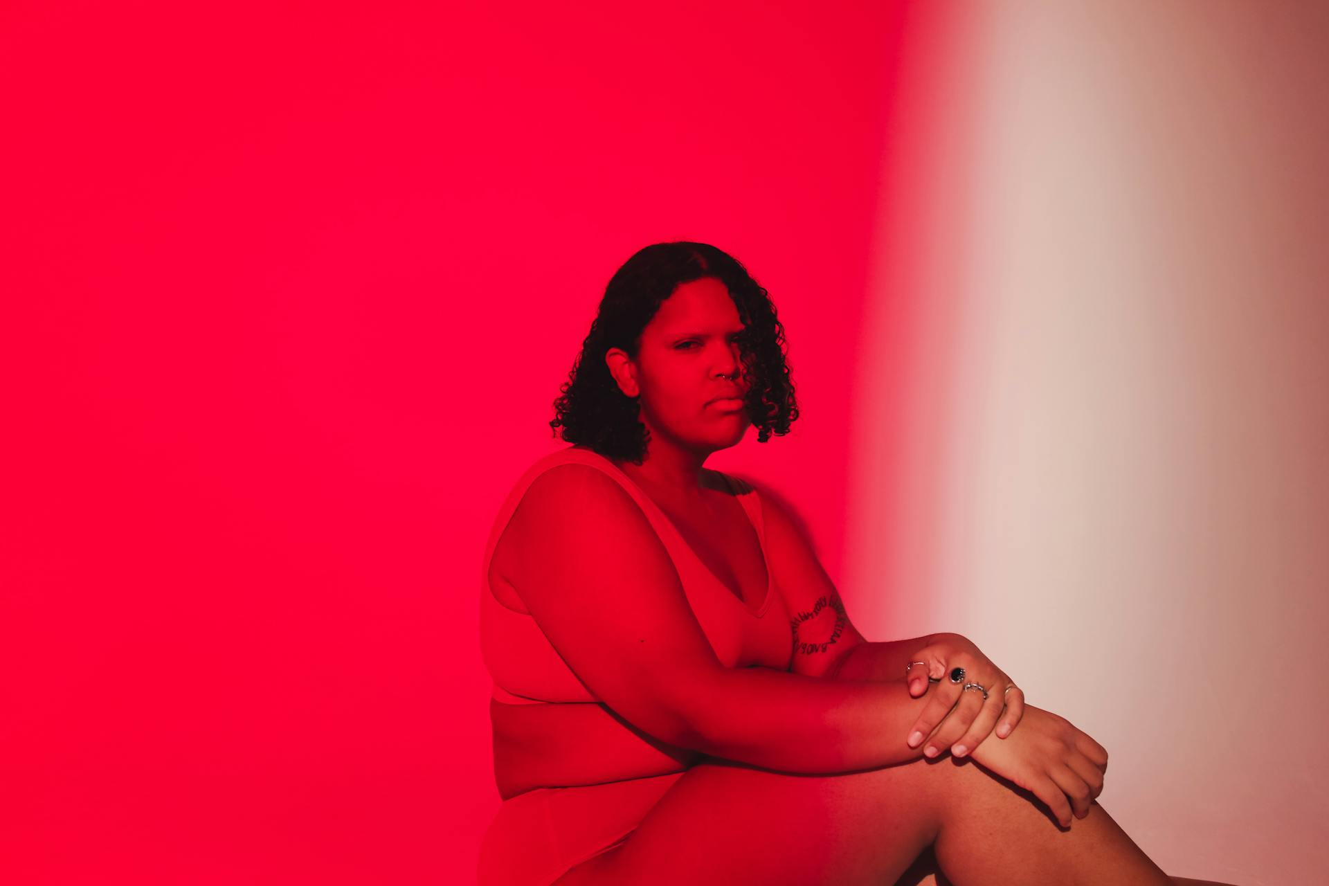 Confident plus size woman seated in vibrant red studio atmosphere, promoting body positivity.