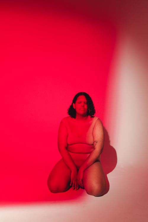 Free Portrait of a confident plus size woman sitting in red studio lighting, embracing body positivity. Stock Photo