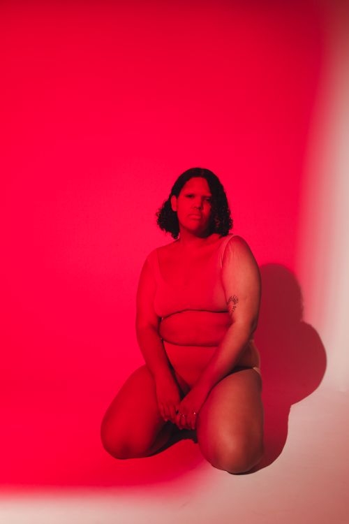 Free Confident plus-size woman kneeling in a red-lit studio, exemplifying body positivity. Stock Photo