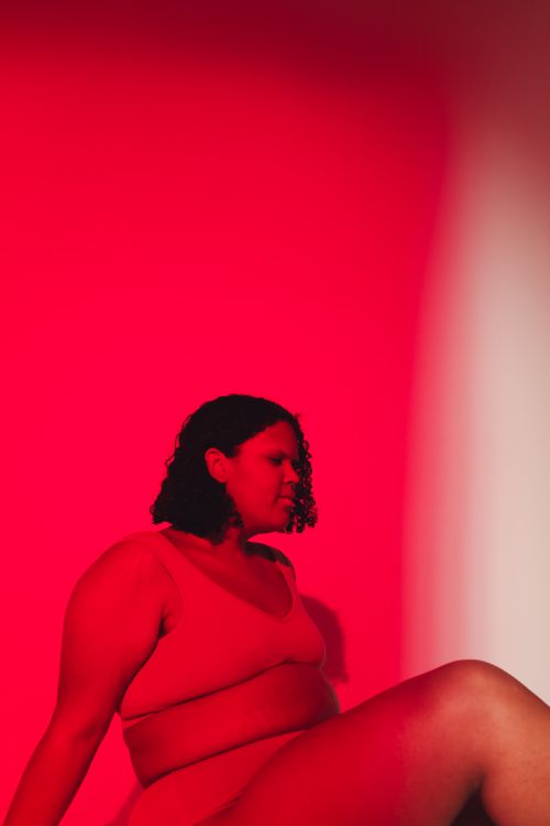 Free Studio shot of a plus size woman embracing body positivity in vibrant red lighting. Stock Photo