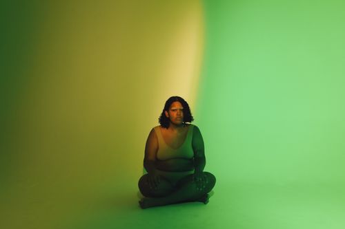 Free Studio shoot of a model embracing body positivity with vibrant green lighting. Stock Photo