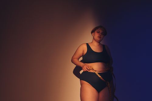 Free A body-positive plus-size woman posing in a studio with a measuring tape, celebrating self-acceptance. Stock Photo