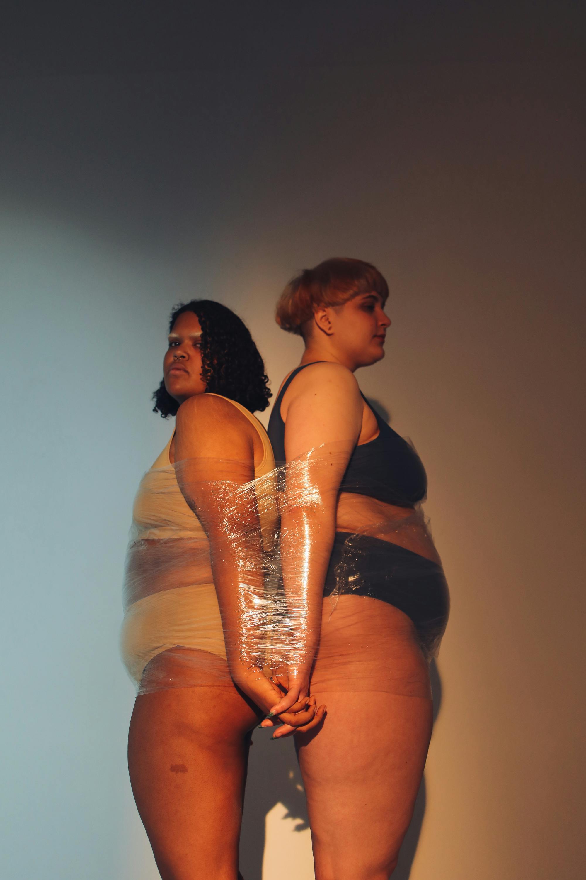 two women standing back to back wrapped with clear film