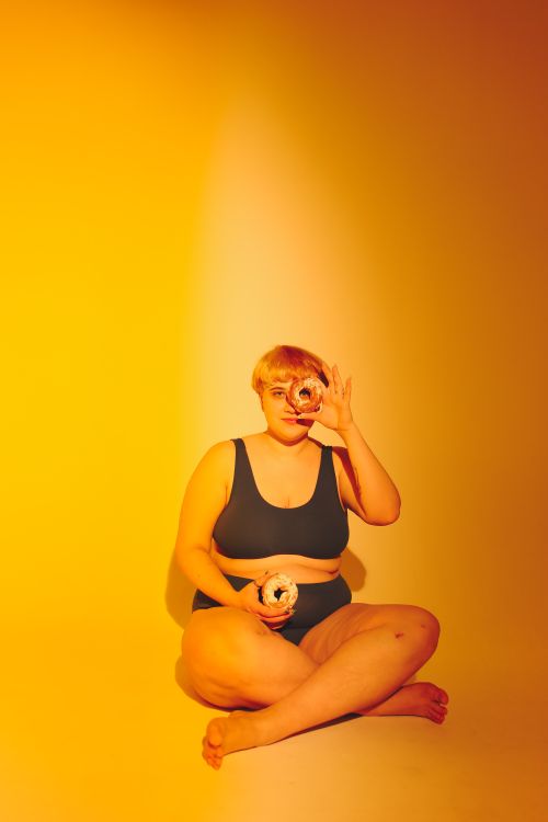 Free A body positive woman holding donuts in a studio with warm yellow lighting. Stock Photo