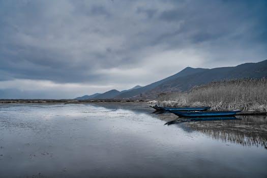 Serene landscape of a lake with boats, mountains in the background under moody skies in China.