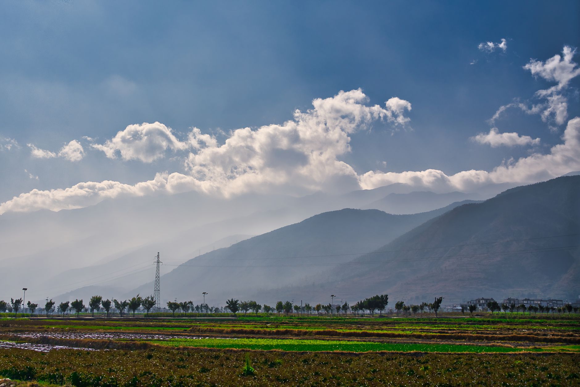 Tranquil landscape showcasing fields and mountains under a cloudy sky in Dali, Yunnan.