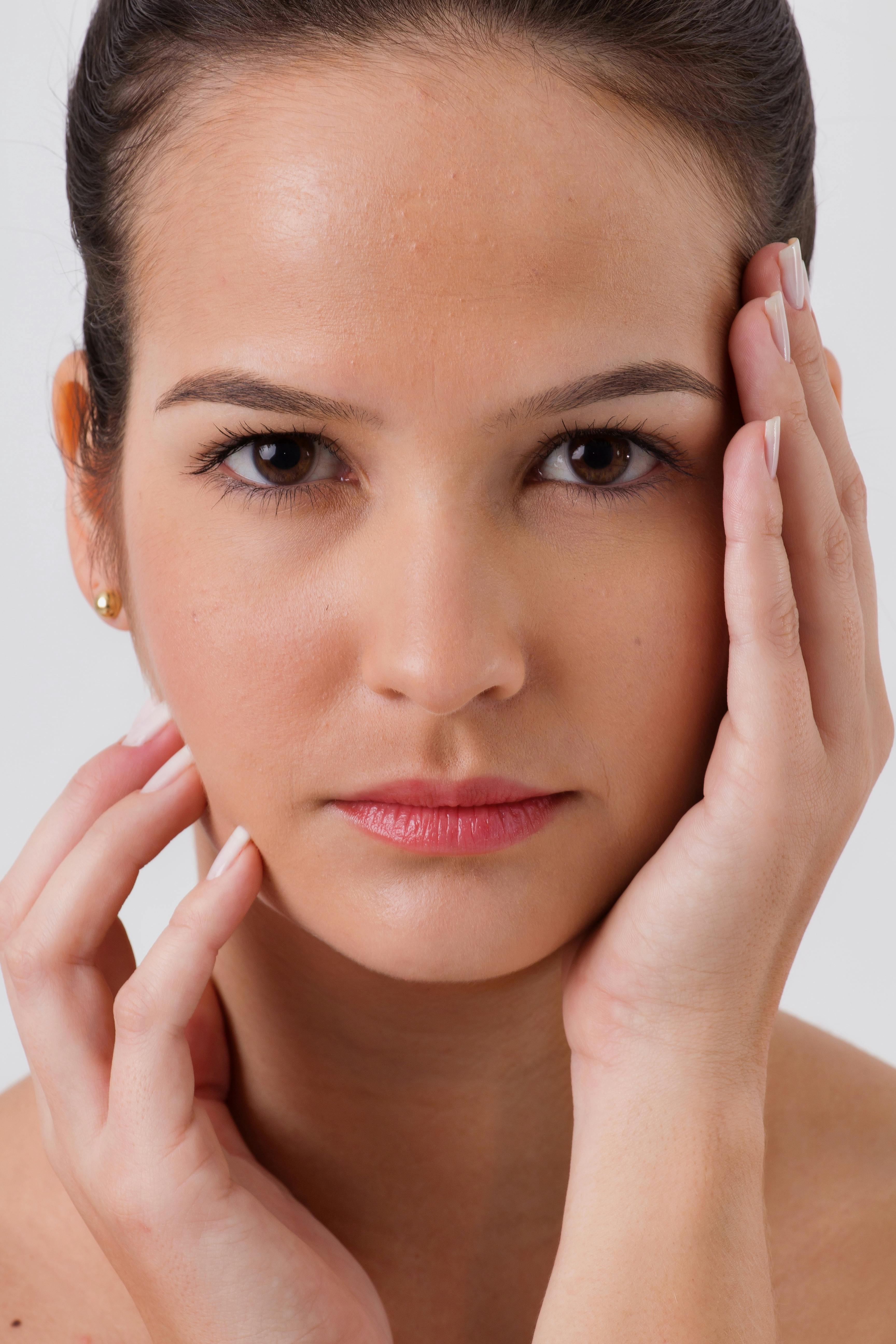 Close-up portrait of a young caucasian woman, hands on face, indoors studio shot.