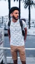 Bearded Man in White and Black Tribal Print Shirt and Brown Shorts Standing on Sidewalk