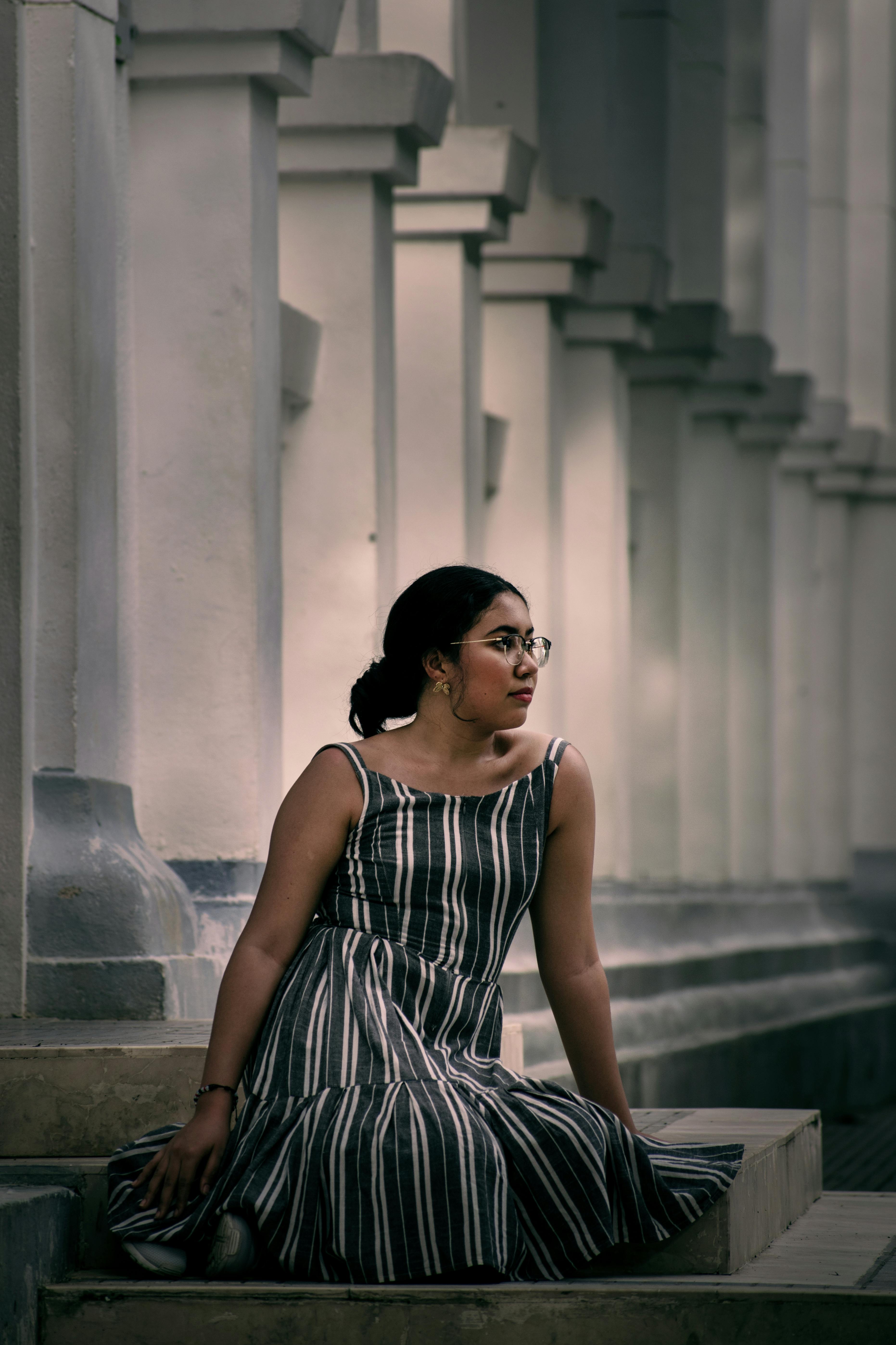 A stylish woman in a striped dress sits on classic steps in an urban setting.