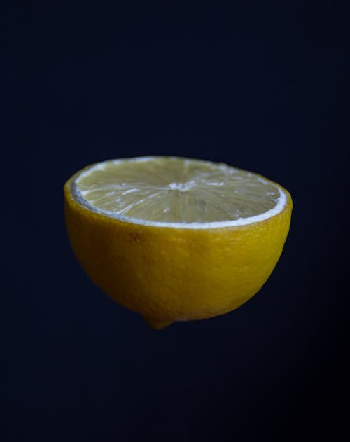 Creative shot of fresh ripe lemon half levitating against dark blue background in studio