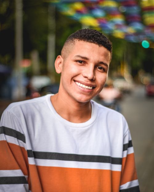 Free Portrait of a smiling young man wearing a striped shirt outdoors with colorful umbrellas in the background. Stock Photo