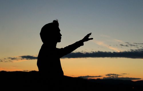 Free Silhouette of a person with raised hand against a vibrant sunset sky, creating a dramatic effect. Stock Photo