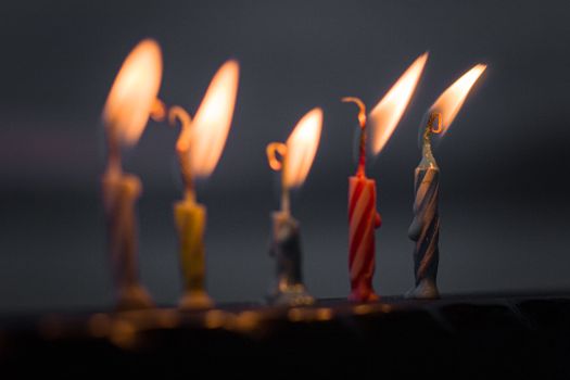 A close-up of illuminated colorful birthday candles in the dark, creating a warm glow.