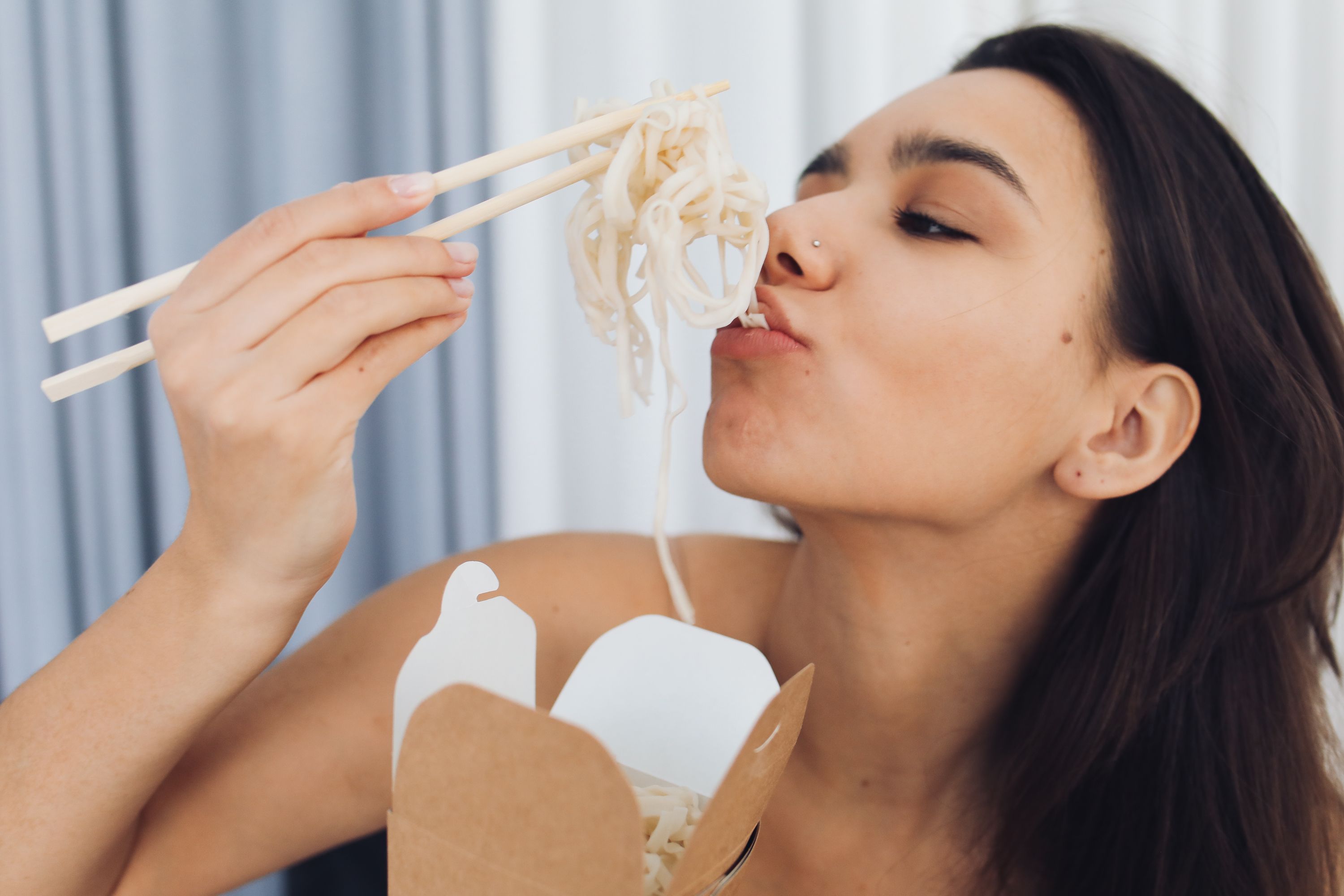 Person using chopsticks to slurp long noodles from ceramic bowl