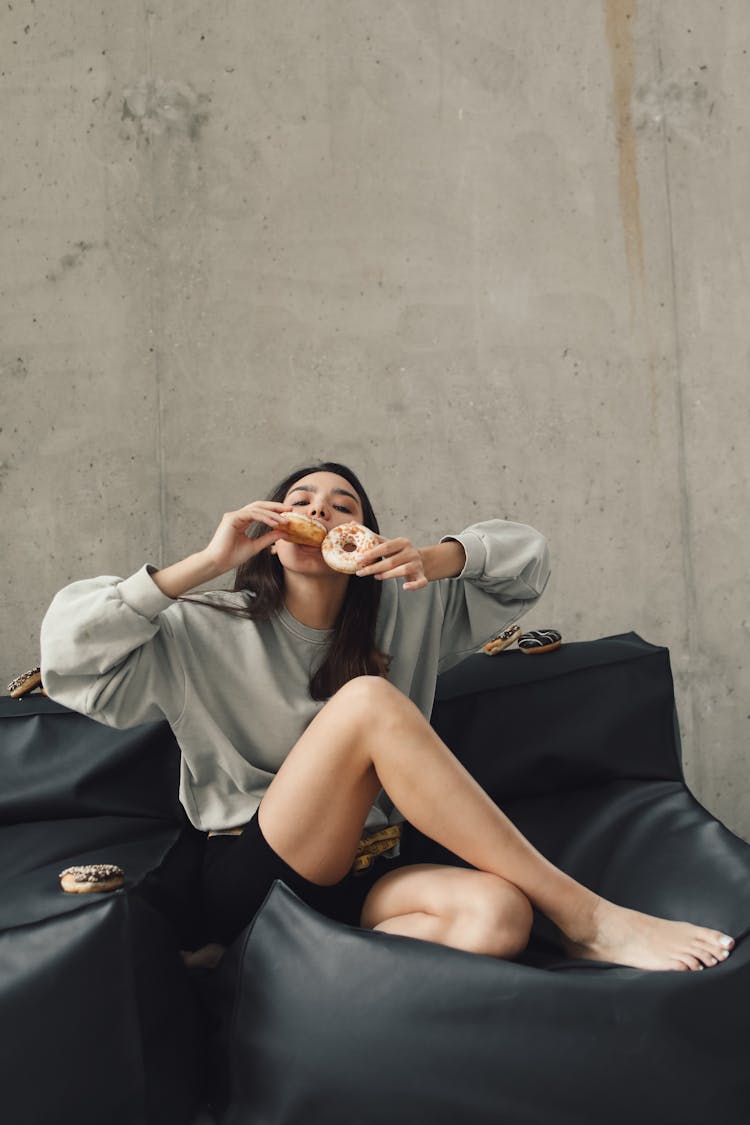 A Young Woman Sitting On Couch Eating Doughnuts