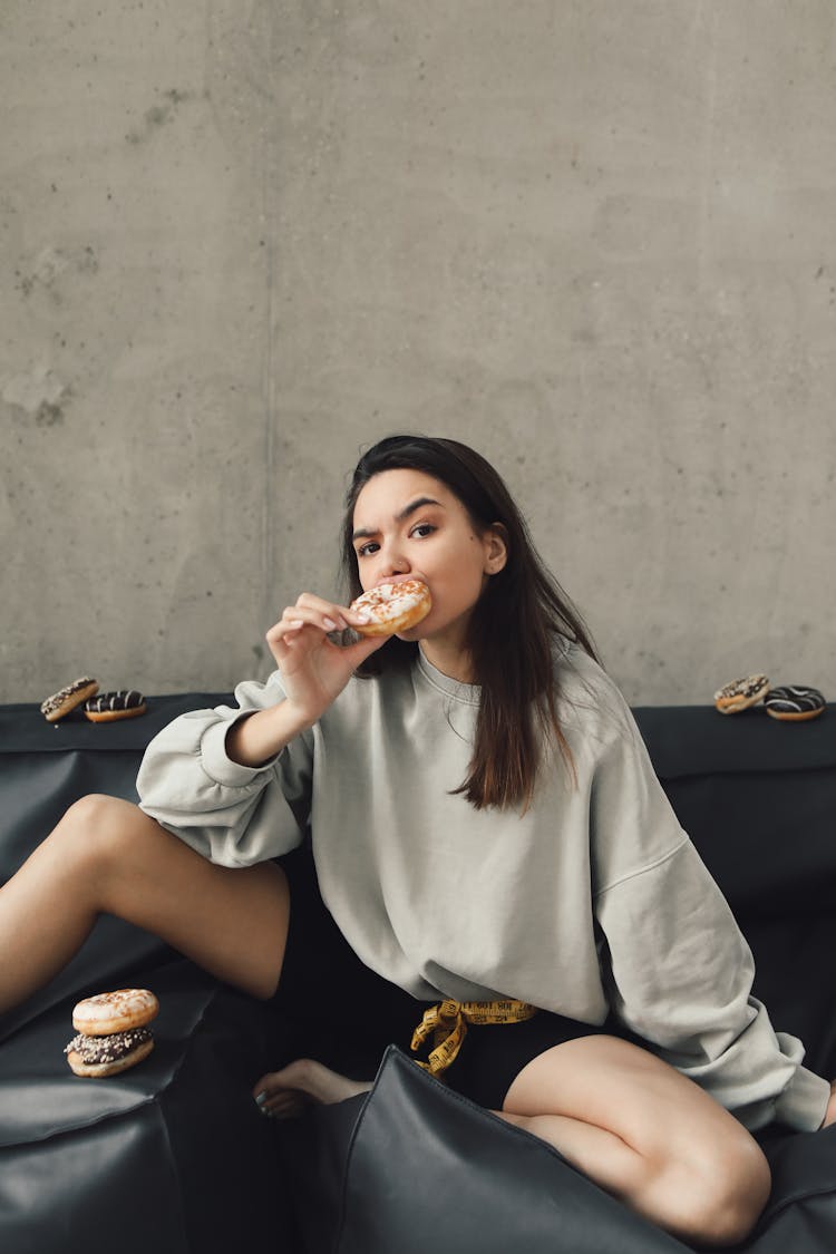 A Woman Posing On A Couch While Eating A Doughnut 