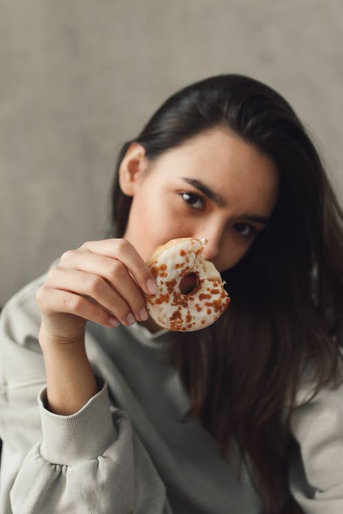 Free Young woman enjoying a donut indoors, showcasing a relaxed and indulgent moment. Stock Photo