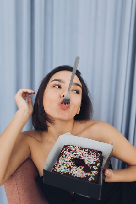 Woman with fork playfully eating chocolate cake with sprinkles.