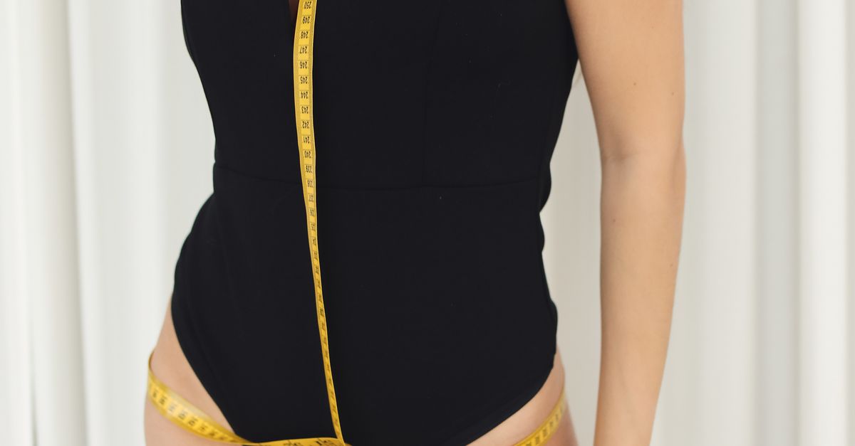 Confident woman in black bodysuit posing with measuring tape, highlighting fashion style.