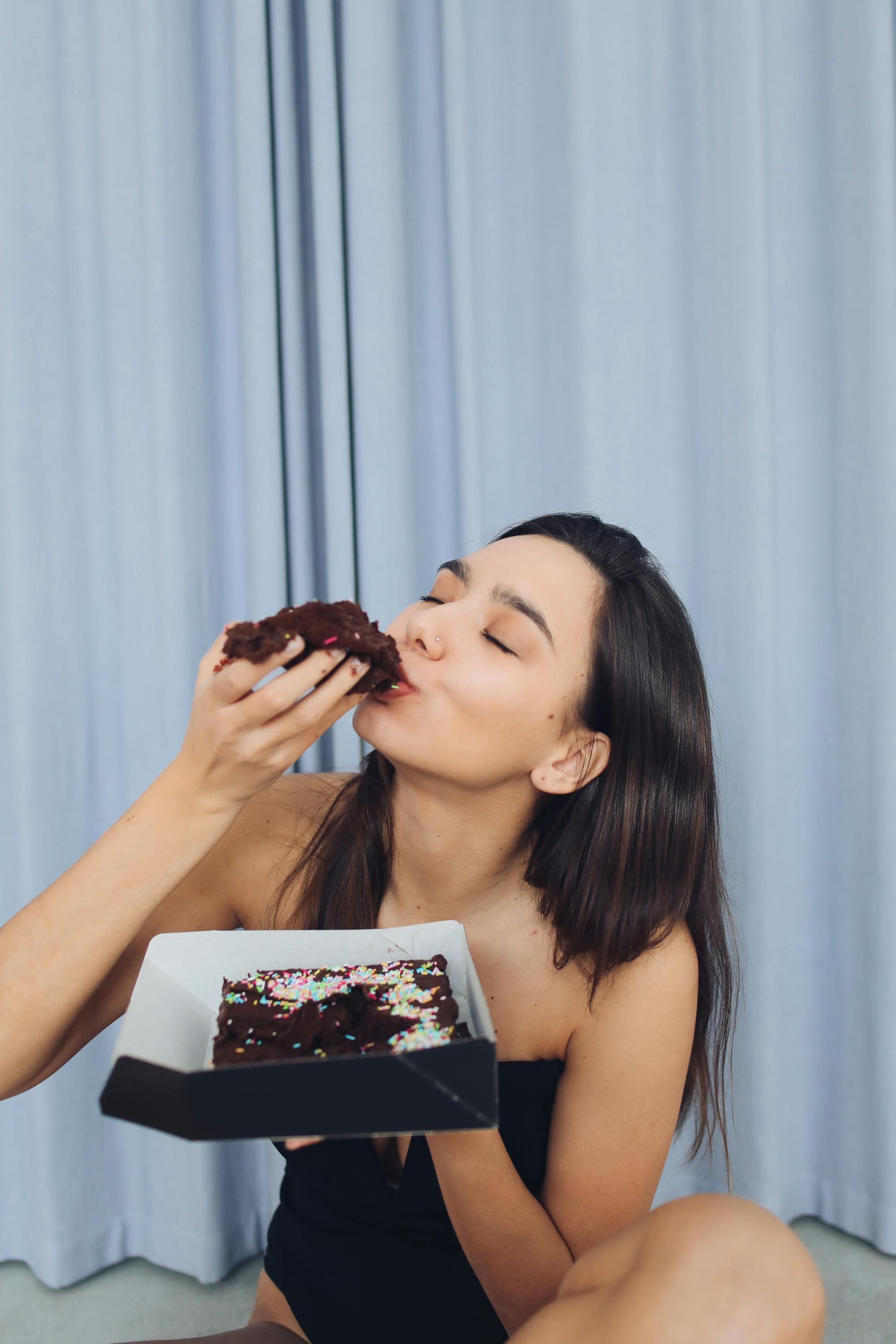 Woman savoring a delicious chocolate cake with sprinkles, eyes closed in enjoyment