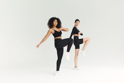 Two women in activewear performing high knees exercise indoors with studio lighting.