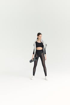 Young woman in stylish activewear holding a yoga mat in a bright studio environment.