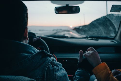 Free Back view of crop anonymous couple of travelers driving modern automobile along asphalt road at sunset Stock Photo