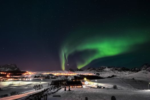 Breathtaking view of aurora borealis illuminating the snowy mountains and village in Nordland, Norway.
