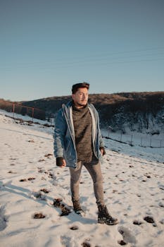 Bearded man in warm clothes walking in snowy outdoor setting with a serene winter backdrop.