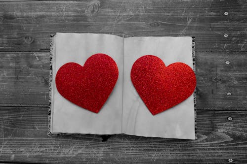 Top view of decorative red paper hearts on white pages of notepad placed on wooden surface during Saint Valentine day