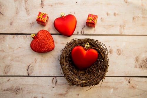 Top view of heart shaped decorations with small decorative gift boxes placed on wooden surface with wicker bowl during Saint Valentine day