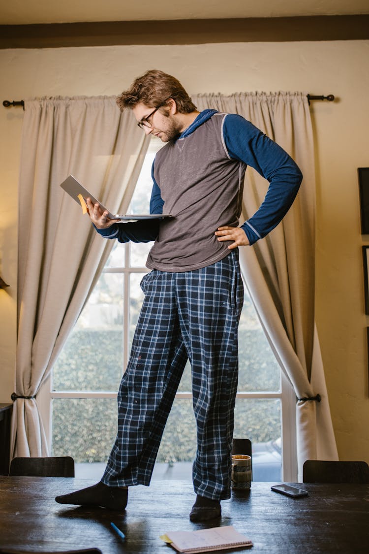 Man Holding A Laptop While Standing On The Wooden Table 