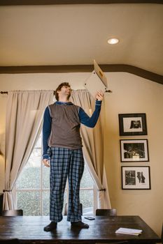 Casual man in pajamas on a table holding a laptop indoors, adding humor and creativity.