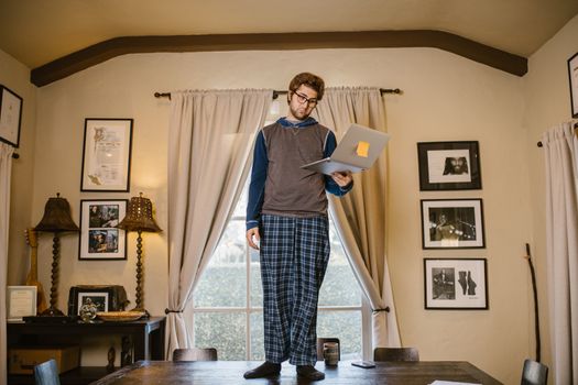 Casual work-from-home setup with a man in pajamas using a laptop on a table.
