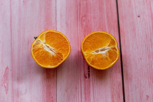 Top view of ripe fresh juicy orange cut in half placed on pink wooden surface in light room in kitchen