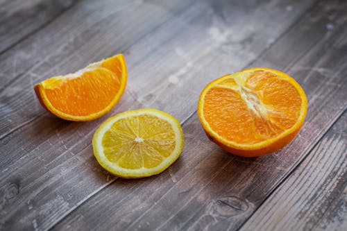 Half and slice of fresh juicy oranges with thin piece of sour lemon placed on wooden surface in light room