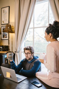 A man and woman working from home using a laptop and coffee mugs in a cozy room.