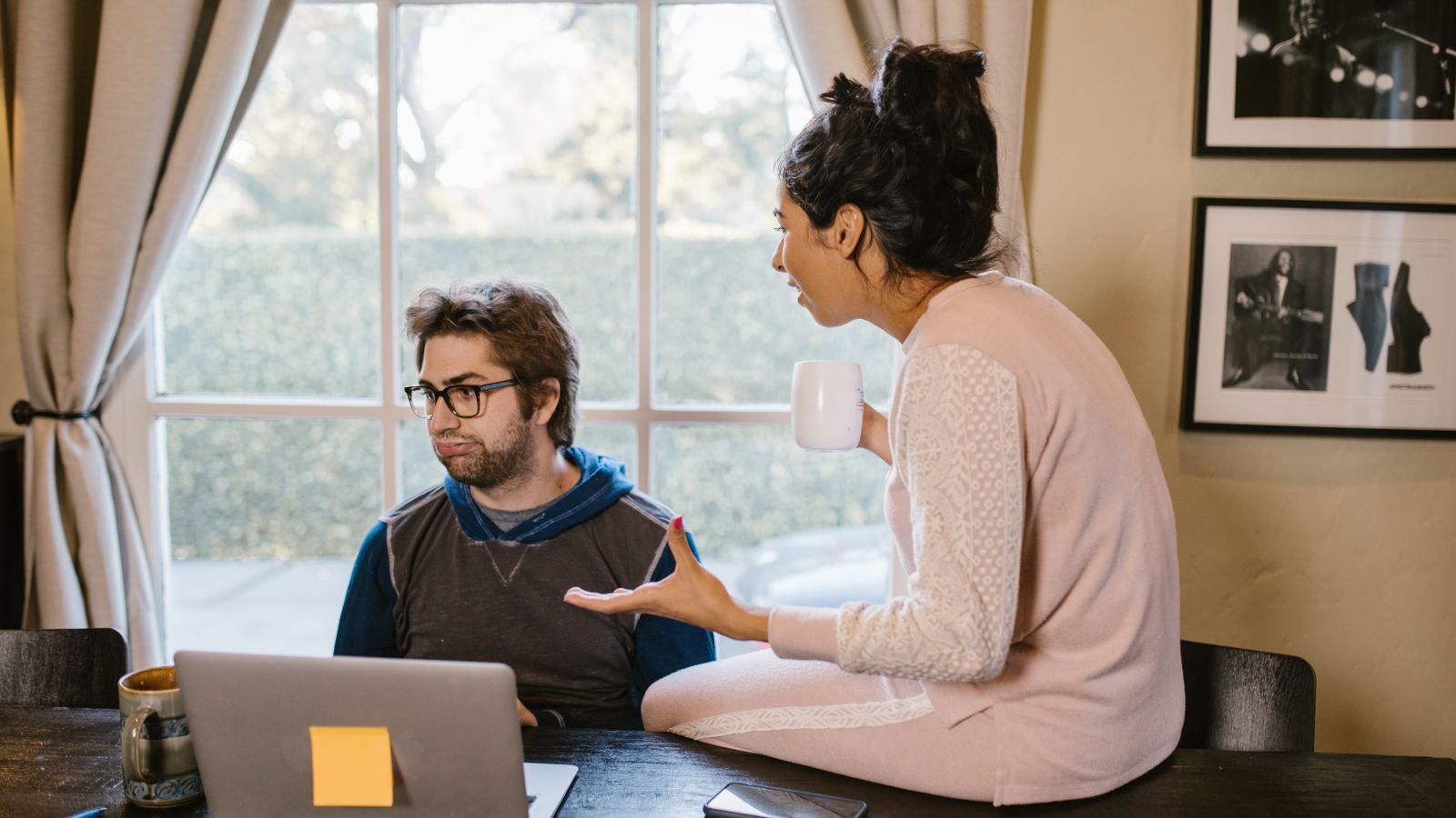 Two adults talking beside a laptop near a window