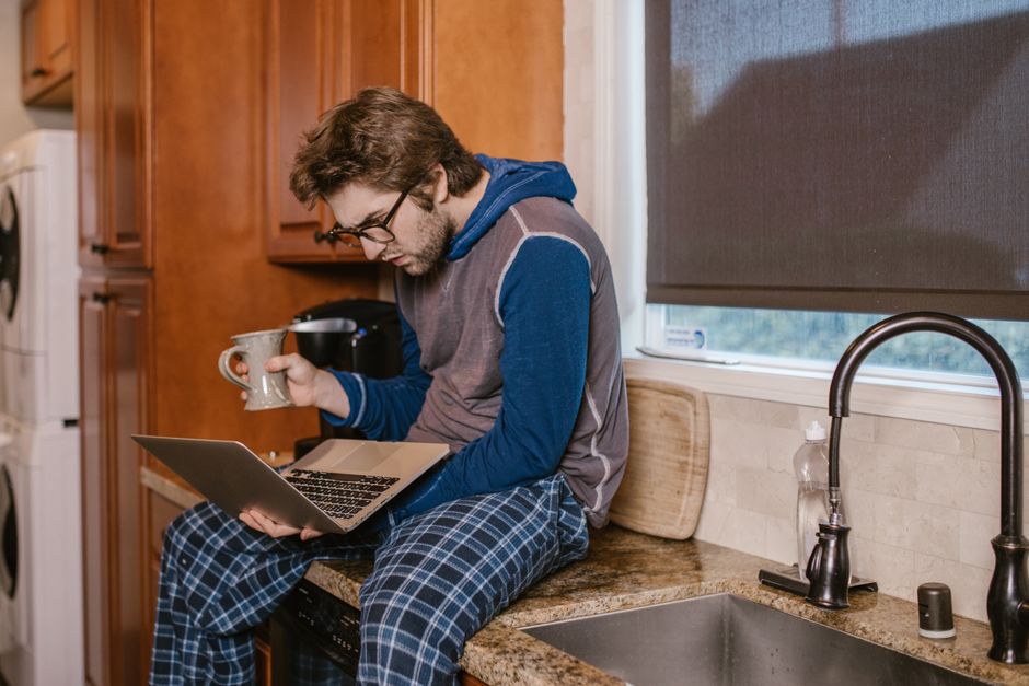 Young man in pajamas studying with a laptop and cup in the kitchen during the day. Young man in pajamas studying with a laptop and cup in the kitchen during the day.