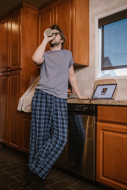 A Man Drinking from a Mug Near a Laptop