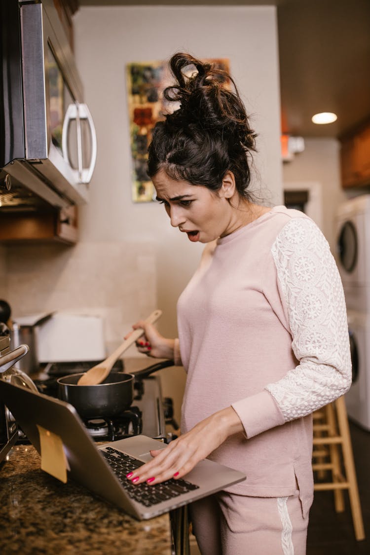 A Woman Looking At A Laptop While Cooking