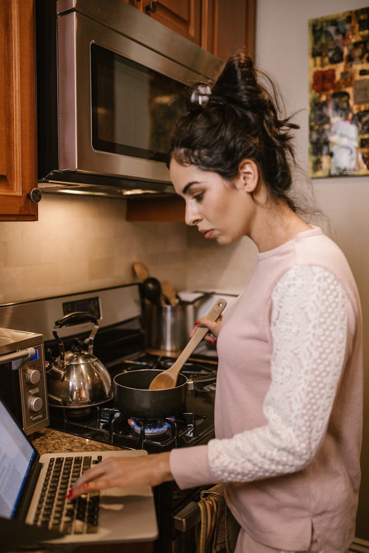 A Woman Typing On Her Laptop While Cooking