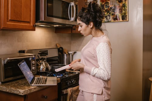 A Woman Standing Near Her Laptop and a Stove