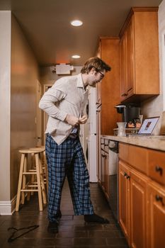 Man in casual attire prepares for an online class in the kitchen, showcasing home learning setup.